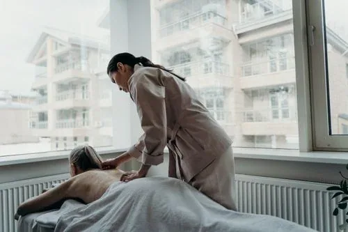 A female massage therapist providing a professional back massage to a towel-draped client
